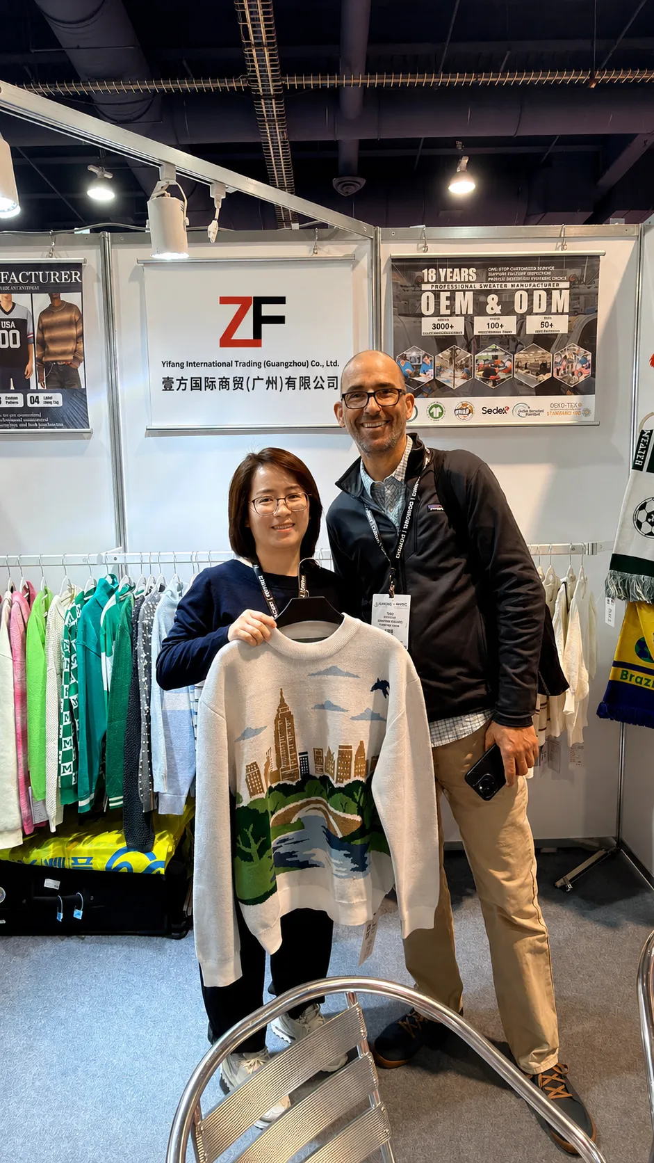 International apparel buyer visiting sweater manufacturer booth and reviewing custom knitwear samples